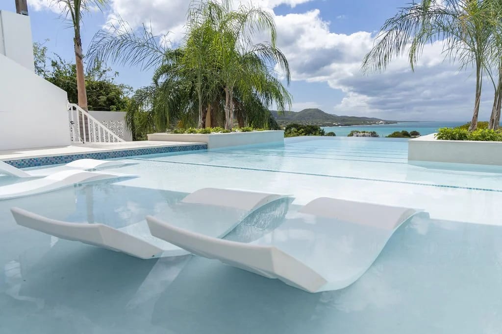 Infinity pool with a built-in lounger ledge, palms and the Caribbean beyond