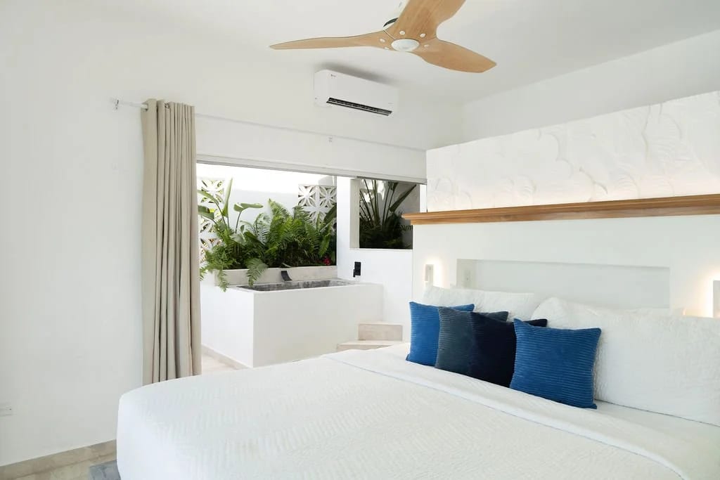 Bedroom with a king bed dressed in white and navy, A/C unit and a planted alcove