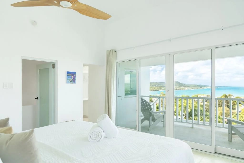 Bright bedroom opening through sliding glass doors to a balcony and ocean view